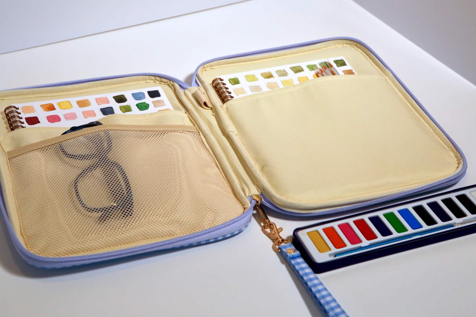 The Juliette Watercolor Clutch open, showing mesh pockets, swatch books, and a colorful watercolor paint set